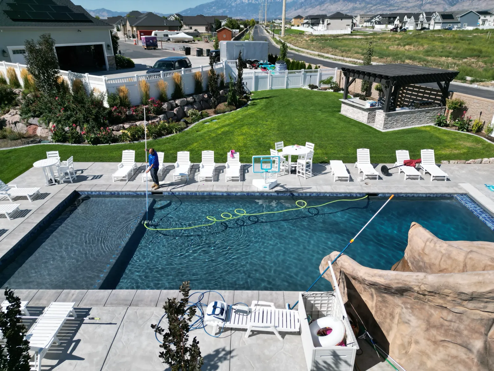 Technician vacuuming a backyard pool with Utah mountains behind