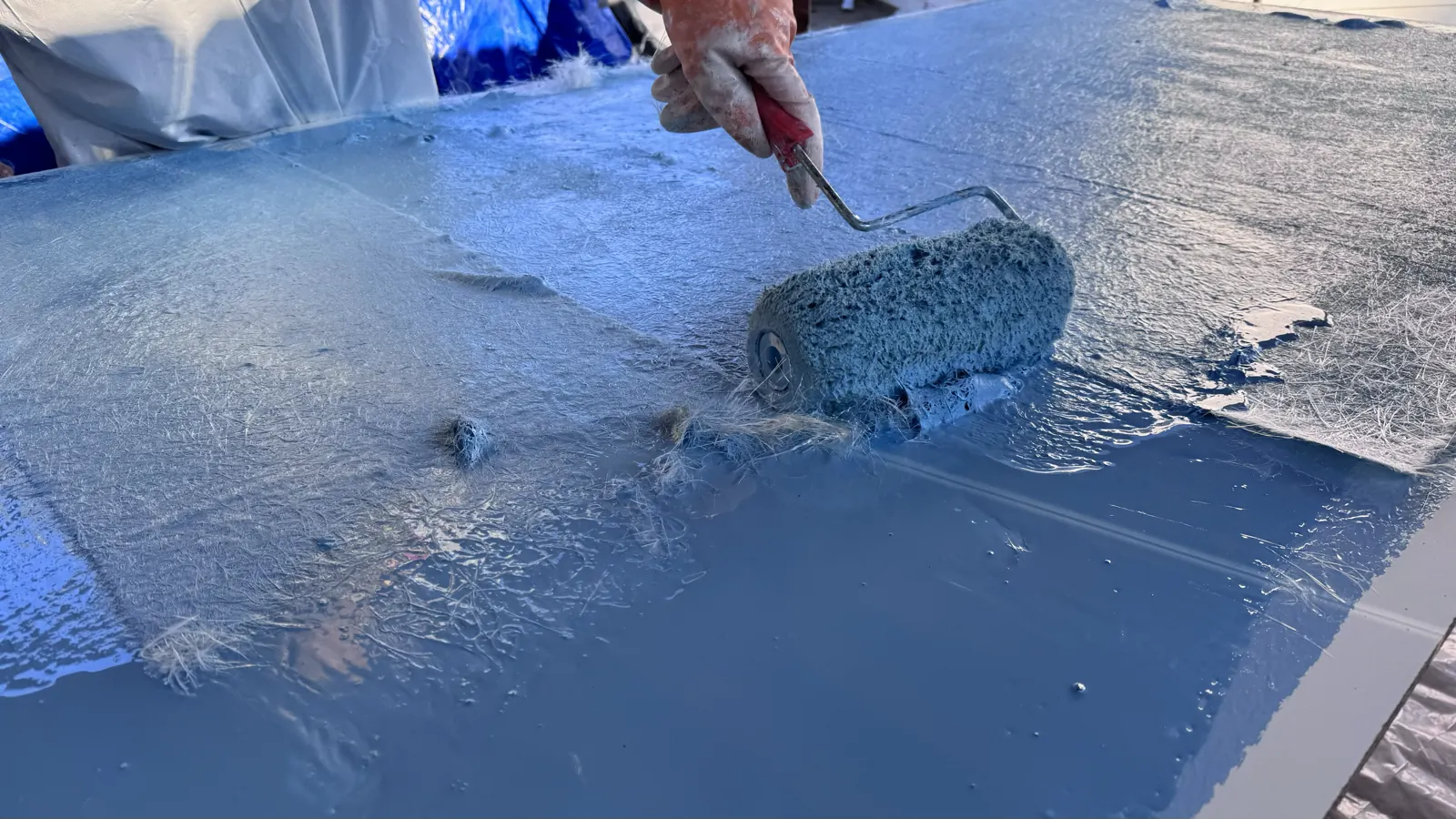 Close-up of a roller applying a blue coat